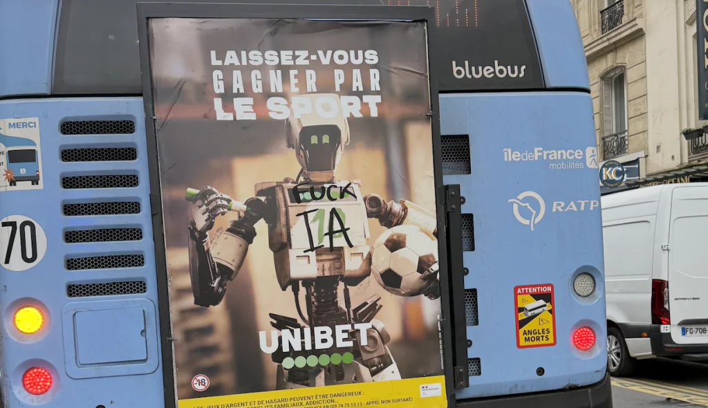 photo d’une publicité sur bus montrant un robot de sport, détournée par un graffiti anti-IA.